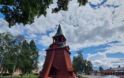 vy över klockstapel rödmålad med grönt koppartak en sommardag