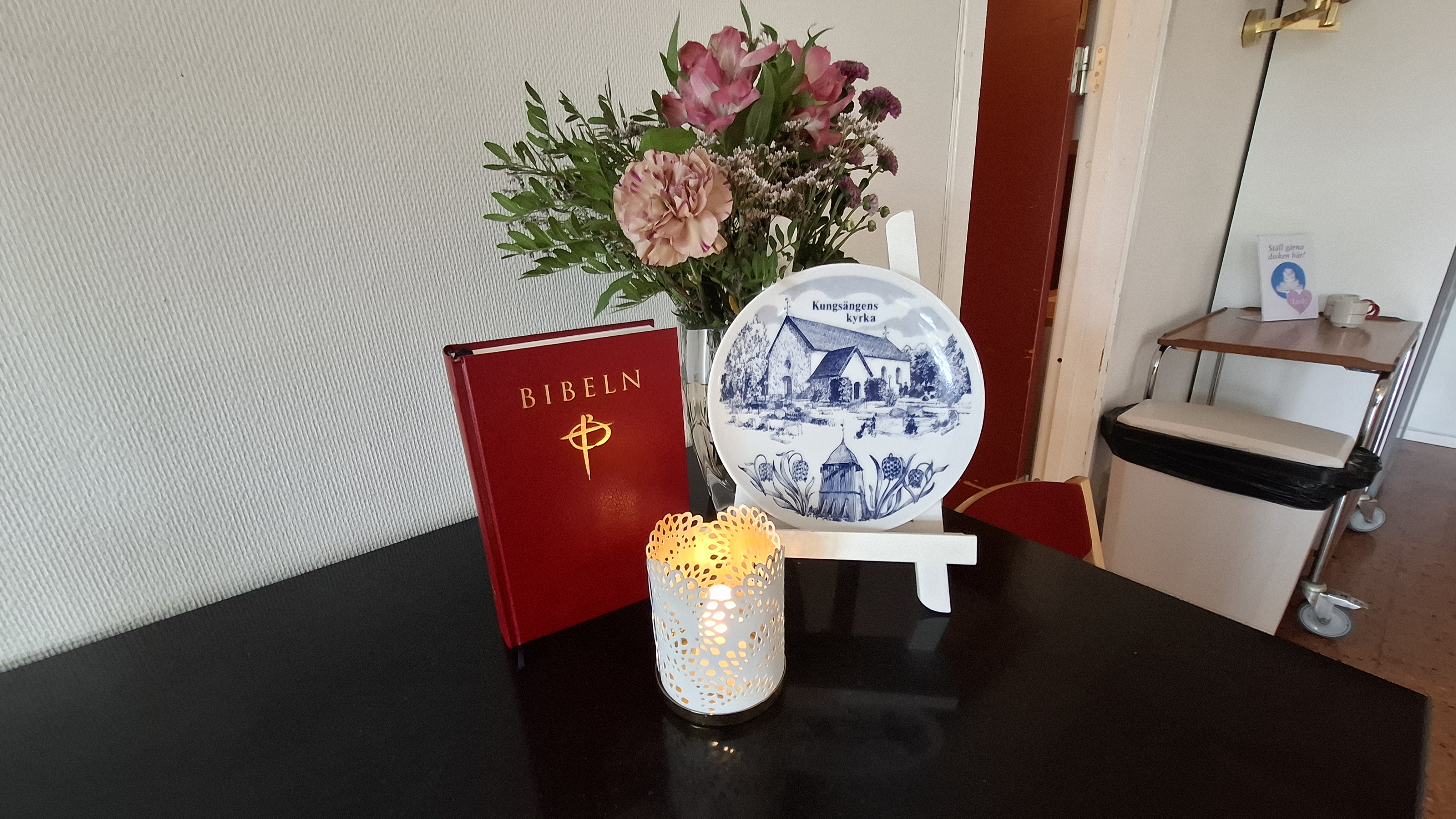 Bibel och tallrik med Kungsängens kyrka på och blommor och ljus