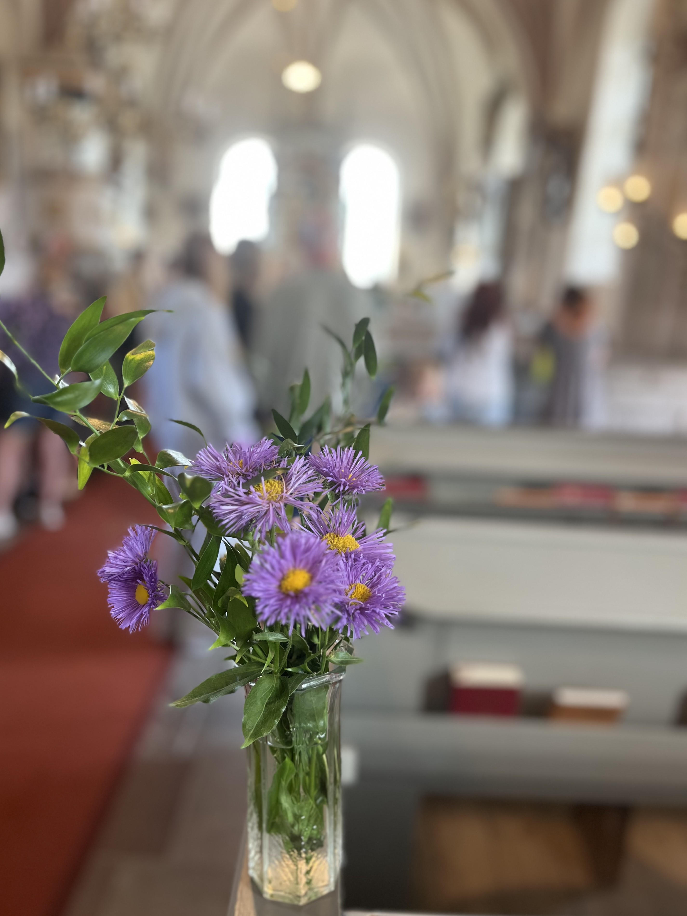 Blommor i vas i kyrkan med besökare i bakgrunden.