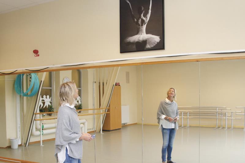 En kvinna tittar mot en tavla föreställande en balettdansare. En spegel täcker hela väggen och kvinnans spegelbild visar henne framifrån. 