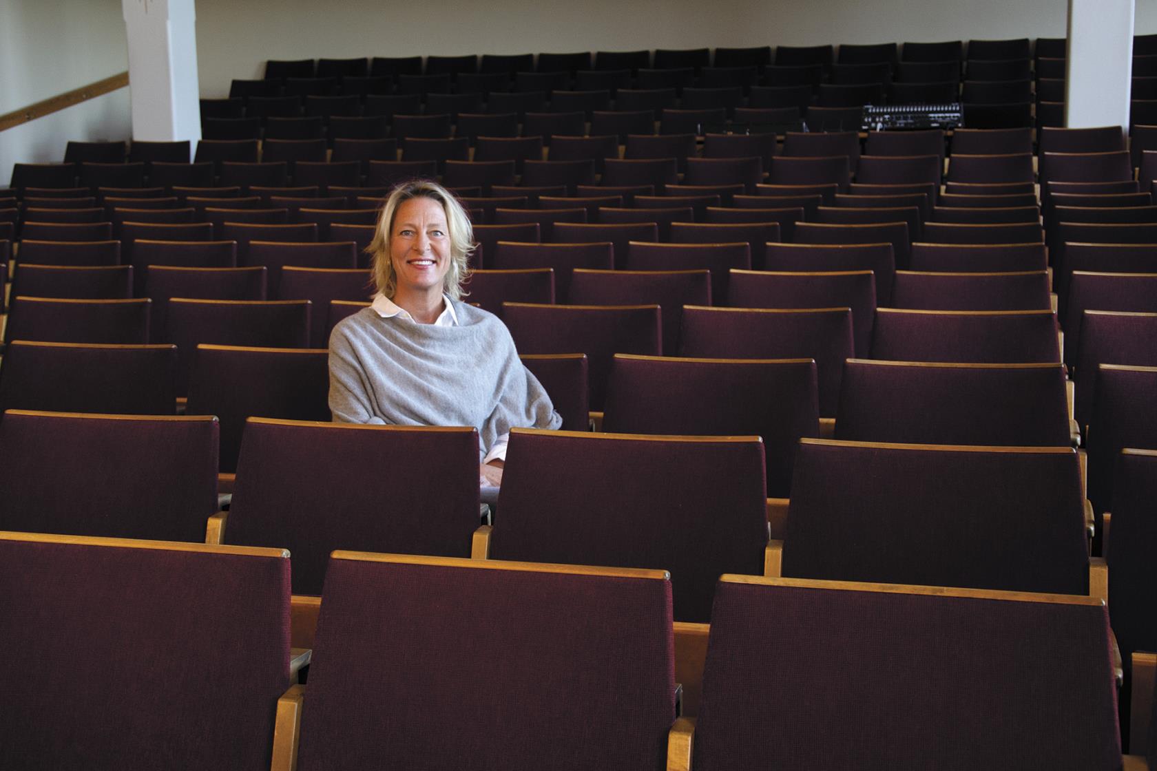 En kvinna sitter i en aula med vinröda stolar