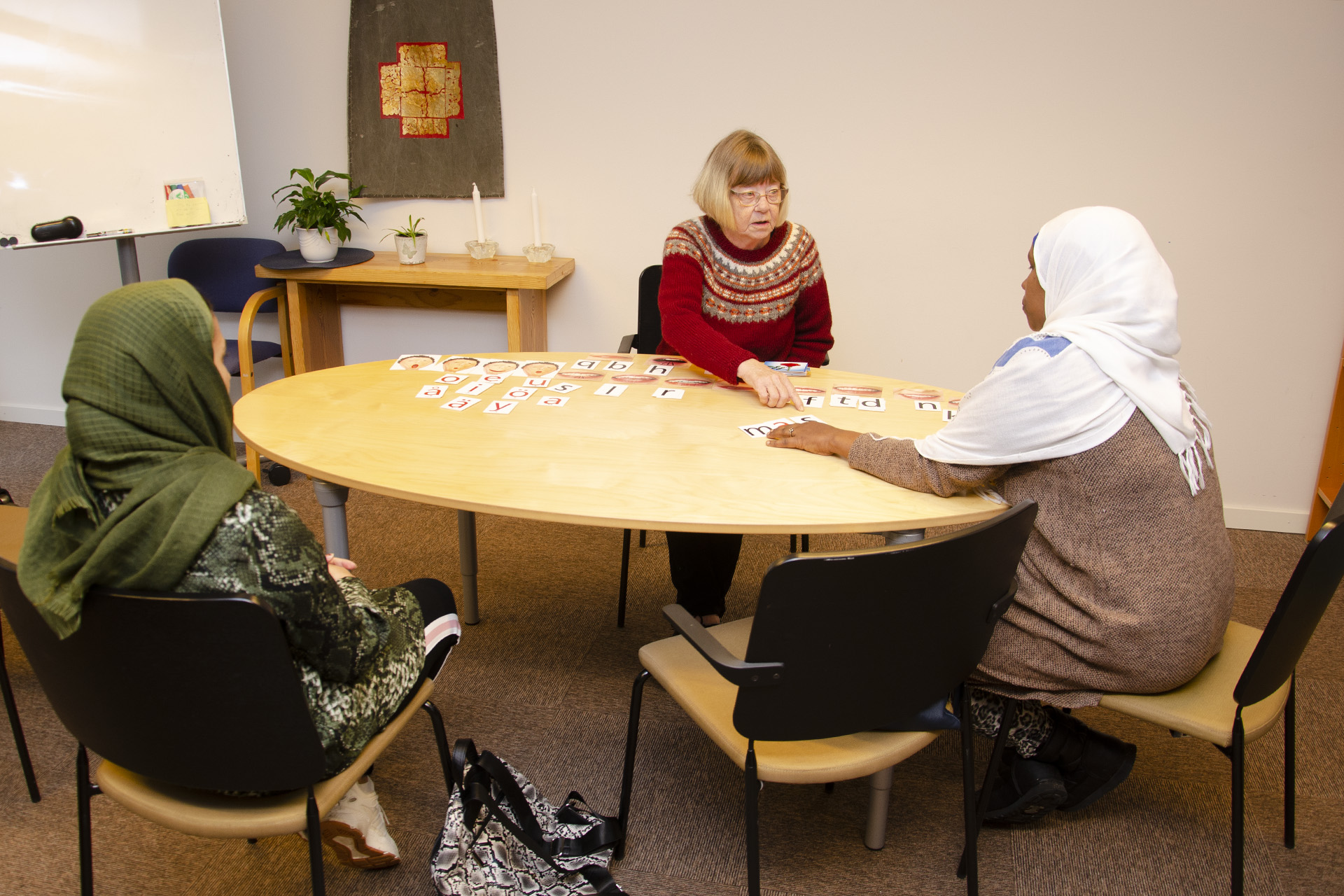 Tre kvinnor runt ett bord. Lappar med bokstäver på bordet. 