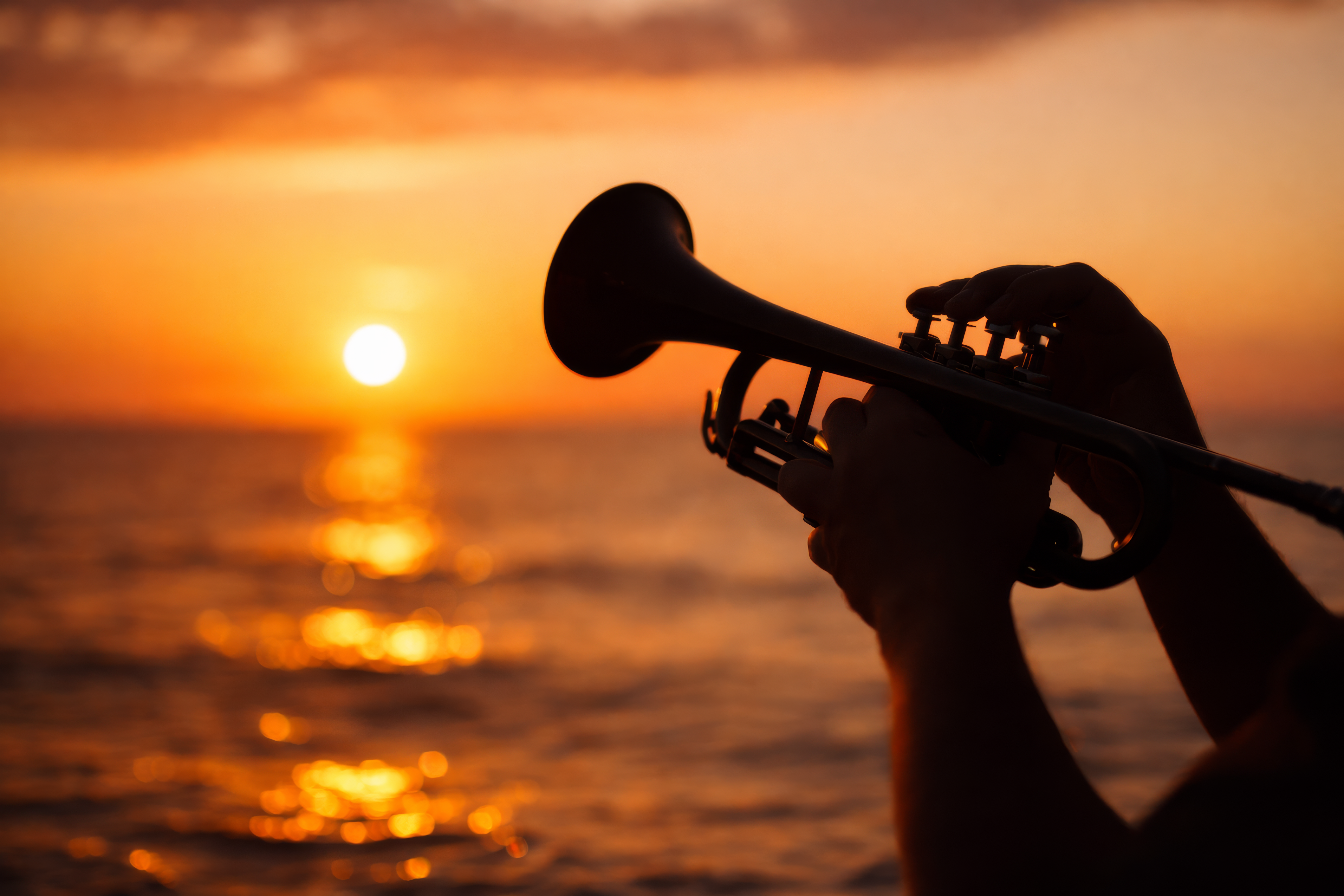 Foto på en trumpet som spelar i en solnedgång över havet