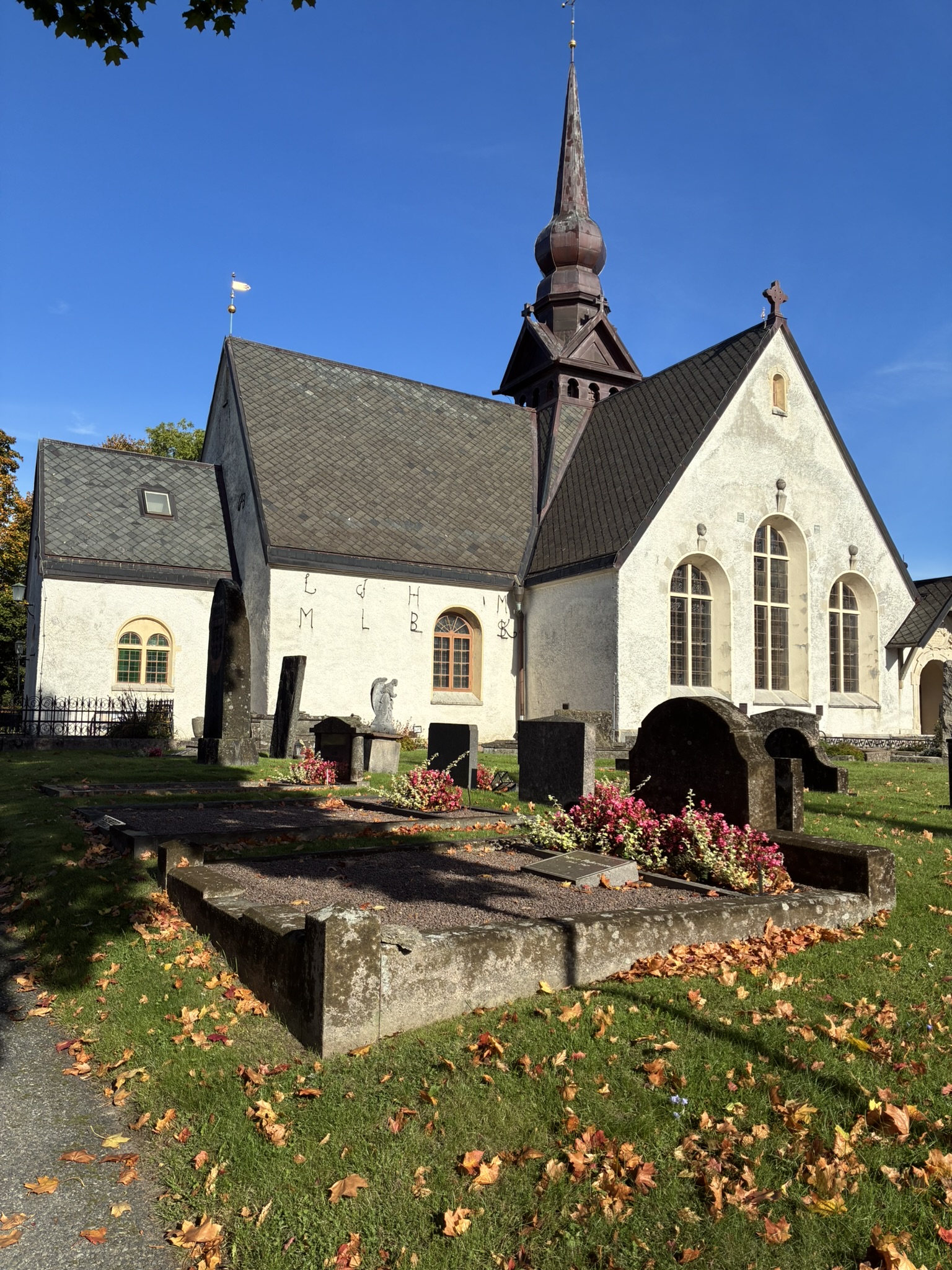 Lerums kyrka i höstsolen med gravplatser och höstlöv