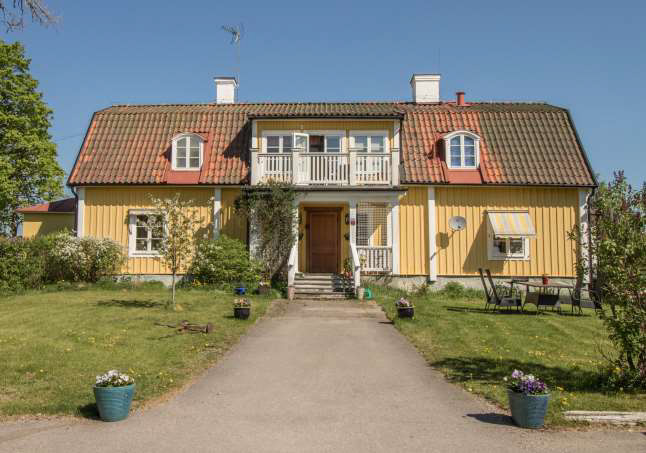 Stor villa med gul träpanel, rött tegeltak, veranda och balkong
