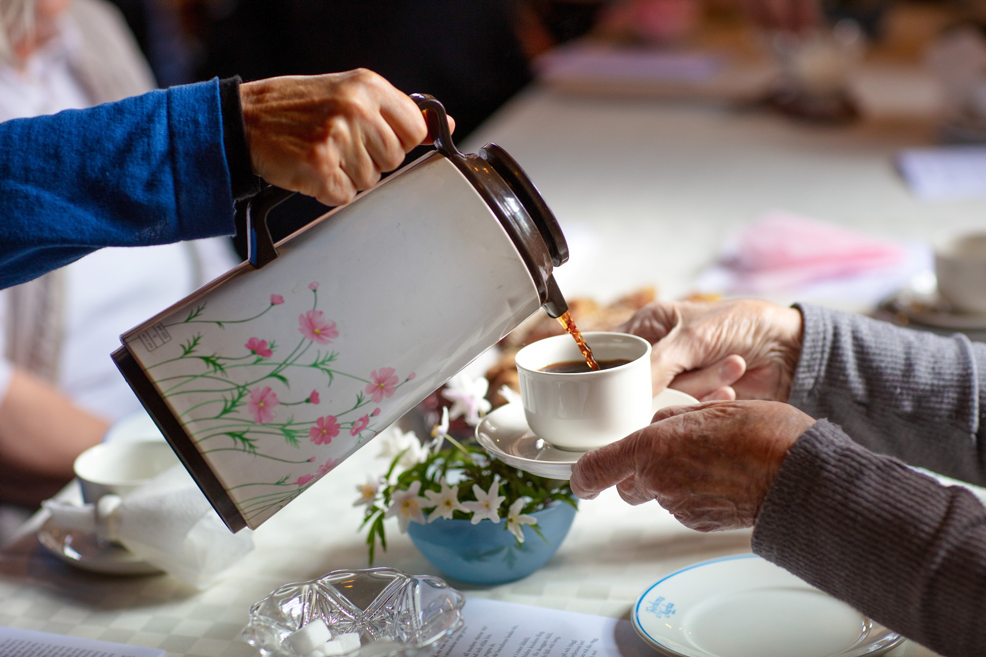 Hand häller kaffe ur en termos åt en person som håller fram sin kopp.