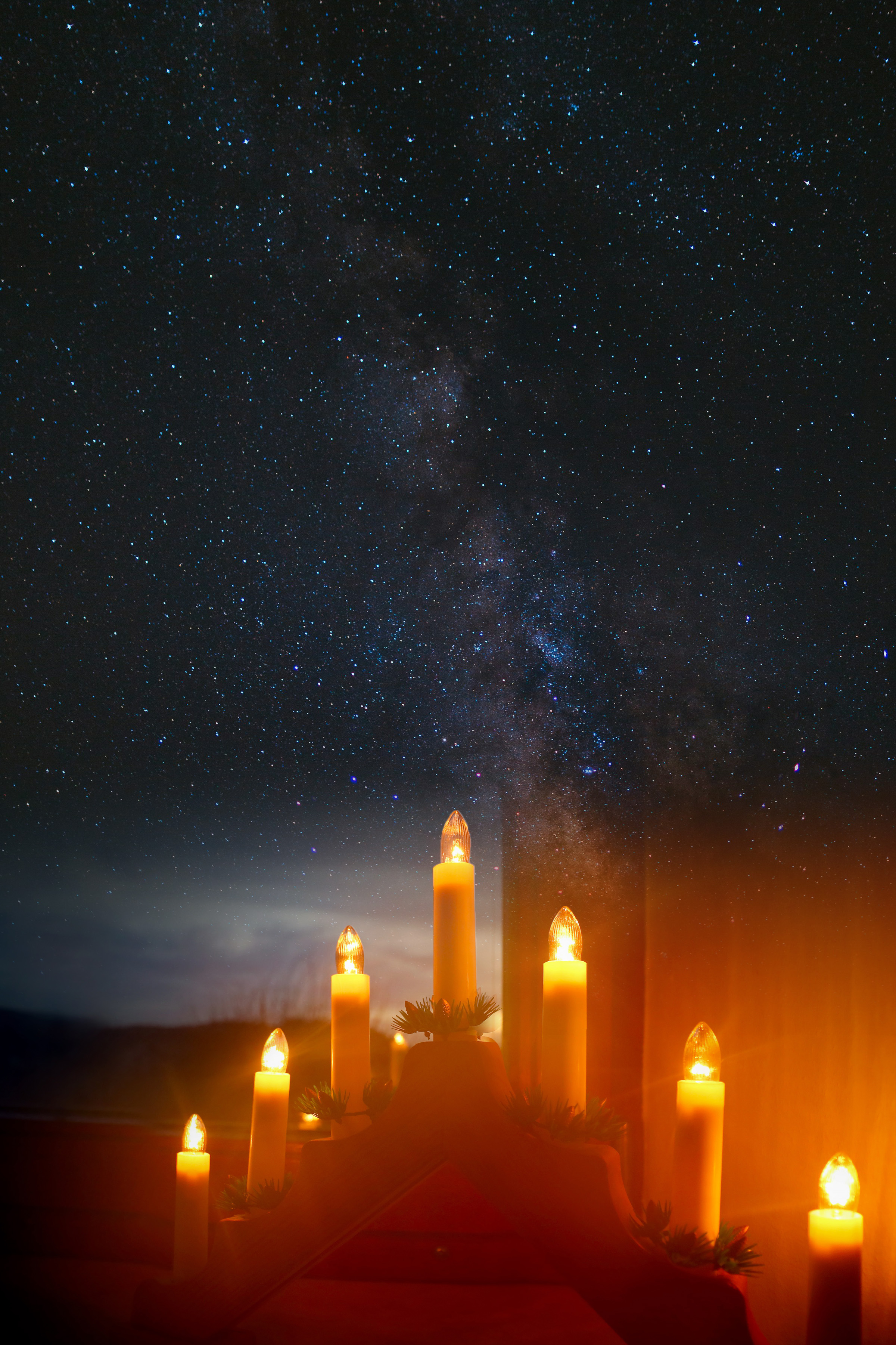 Adventsljusstake i fönster mot svart rymd.