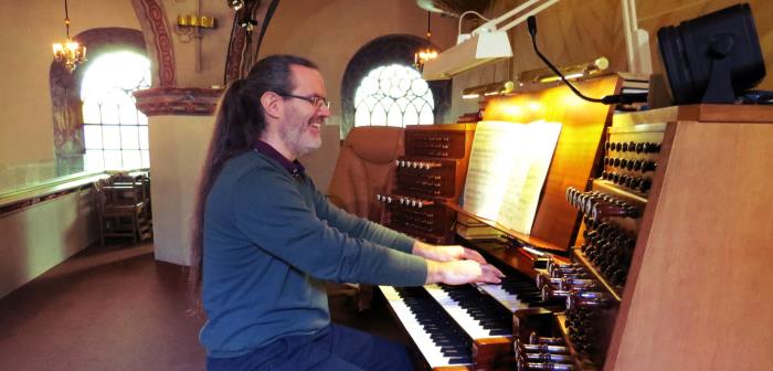 Man med hästsvans spelar på kyrkorgel.
