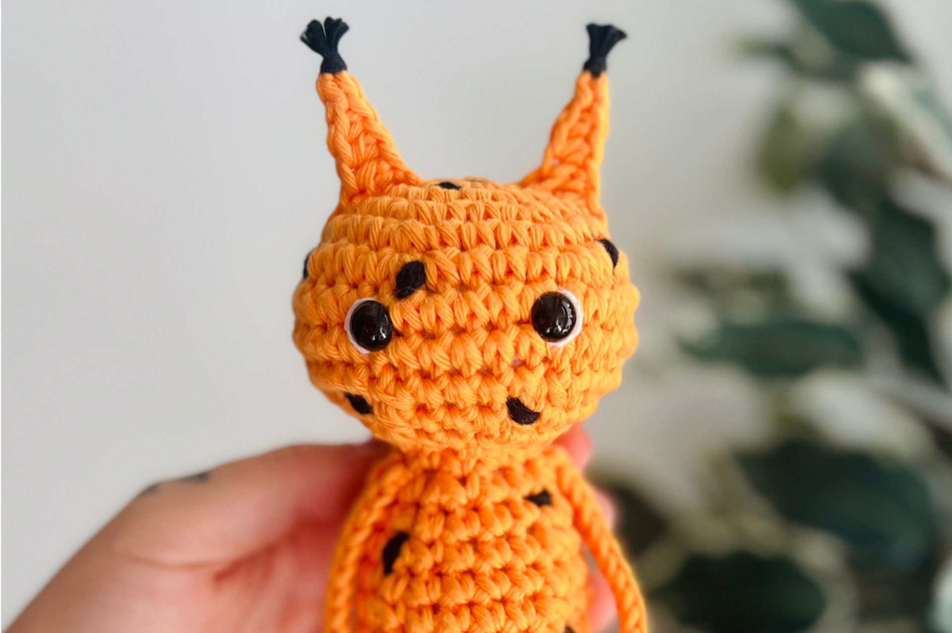Hand håller liten orange virkad figur.