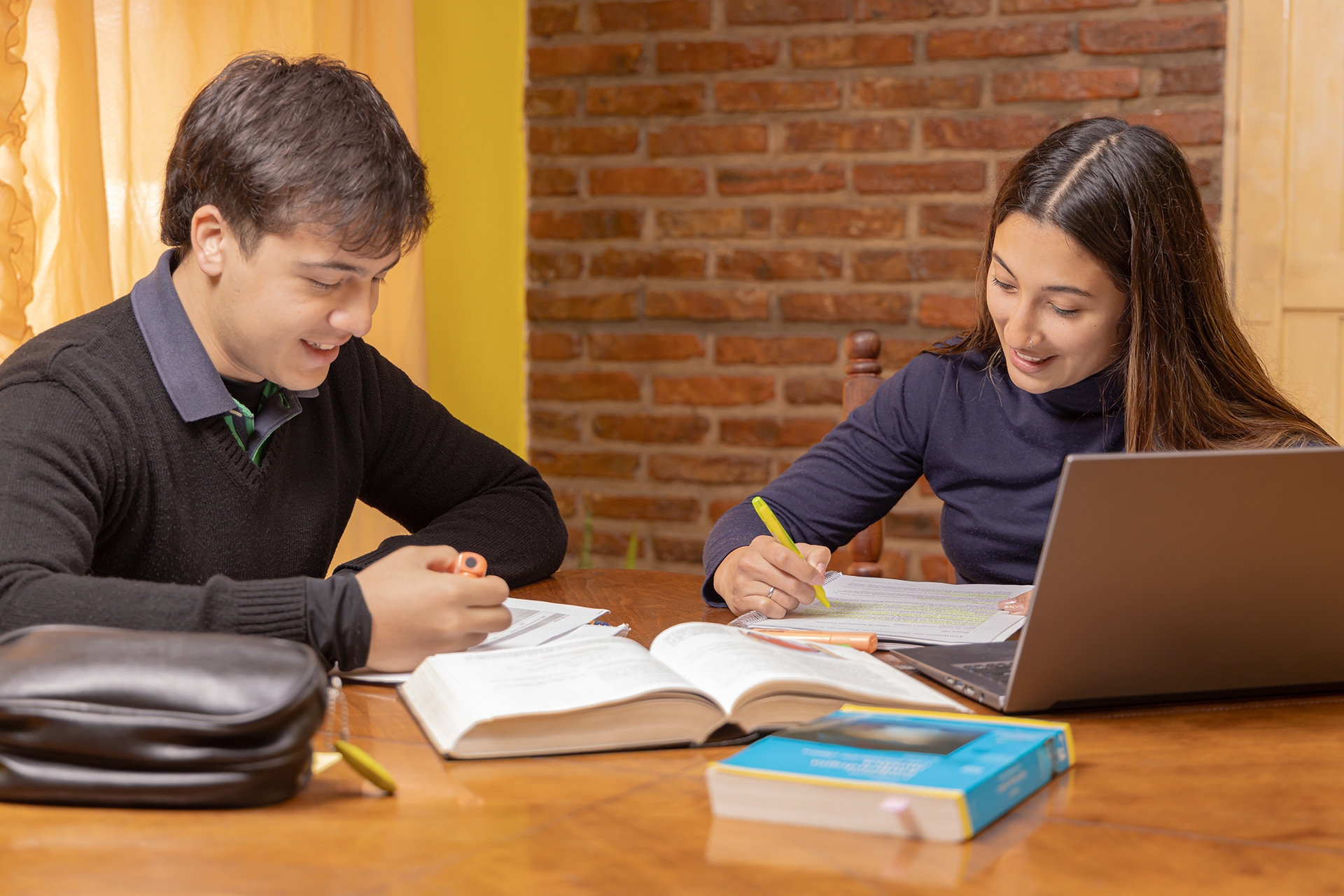 Två ungdomar läser läxor. Framför dem på bordet ligger bland annat böcker och en laptop.