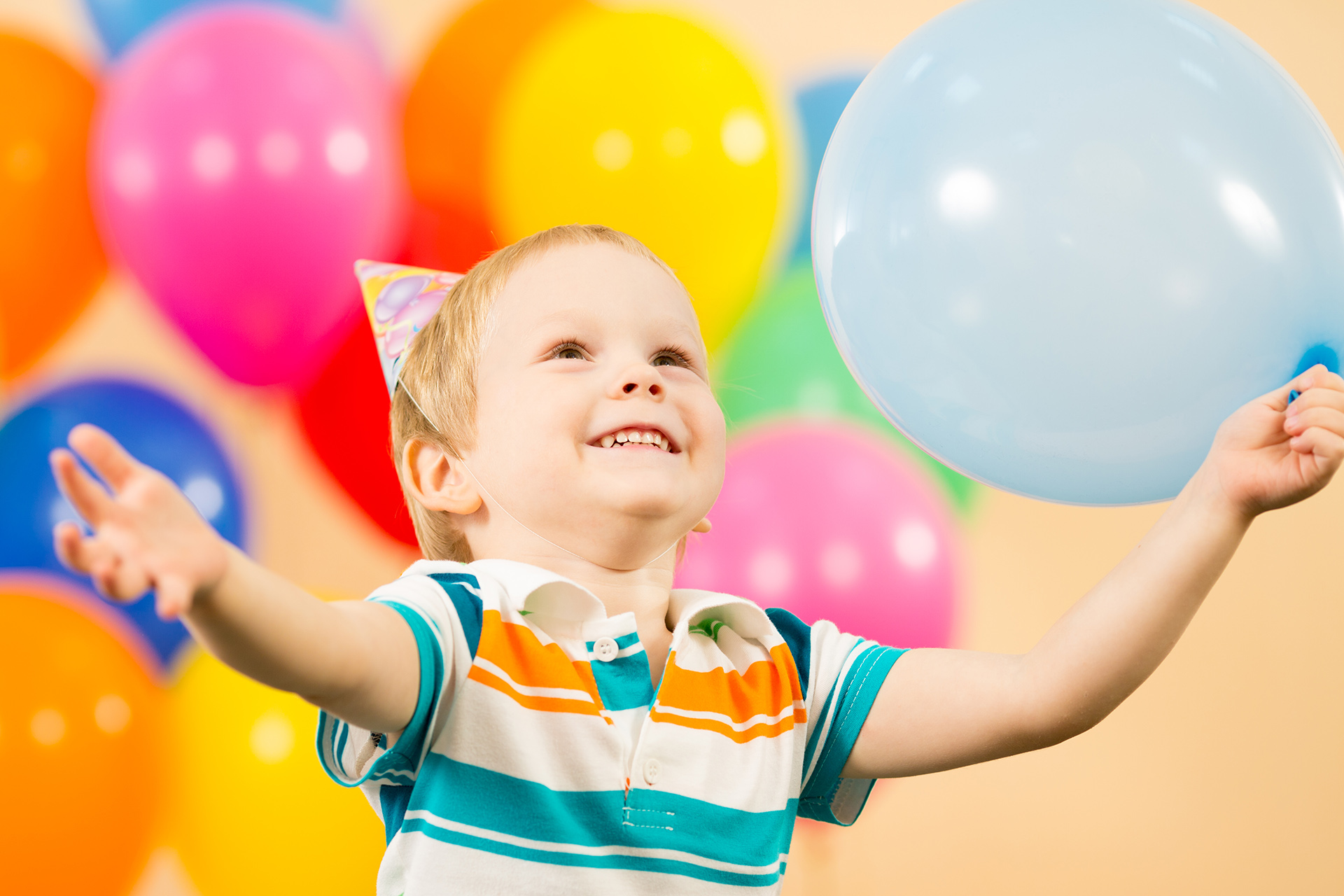 Glad pojke omgiven av färgglada ballonger.