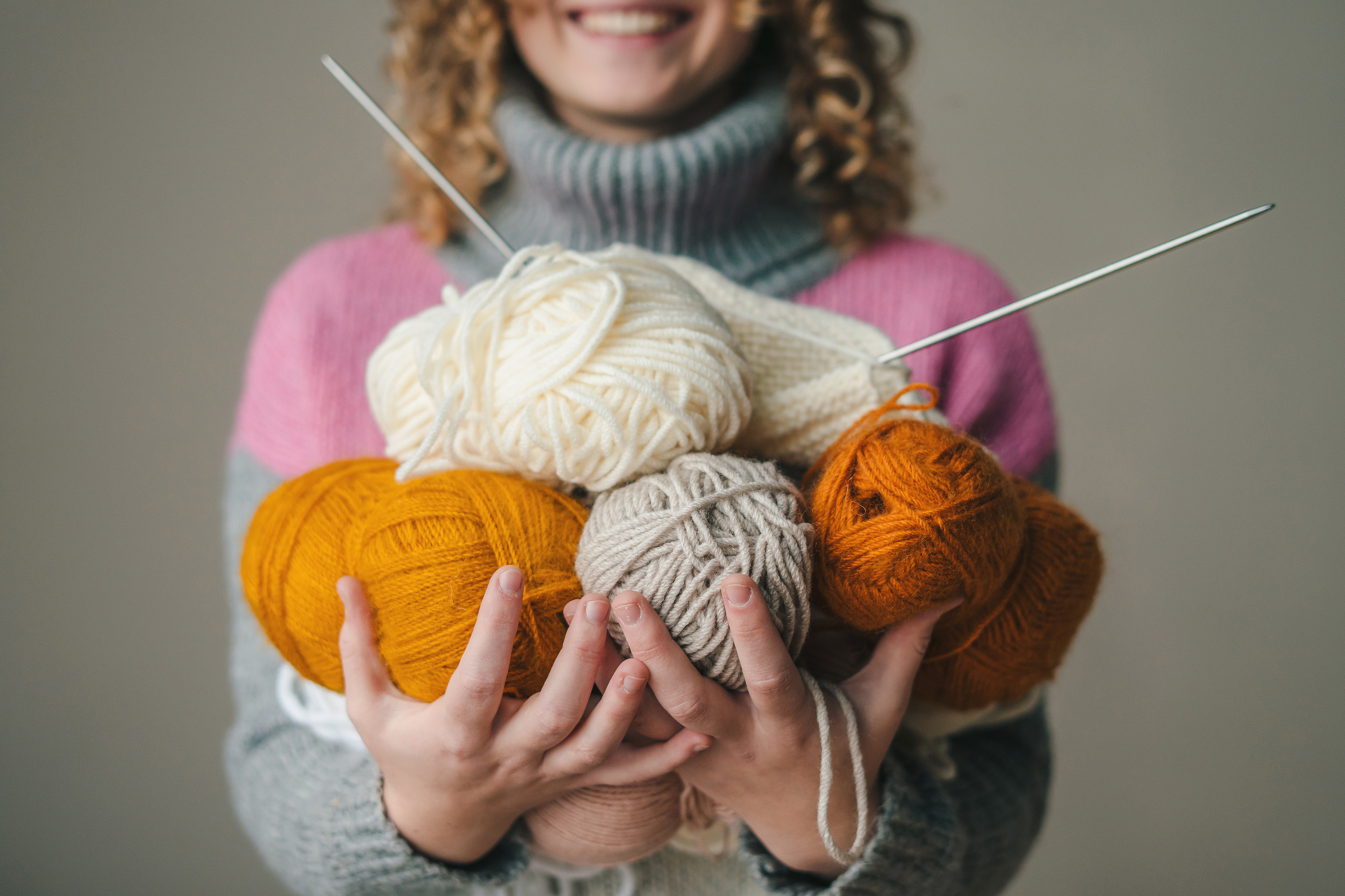 En person håller flera garnnystan samt ett par stickor i händerna.