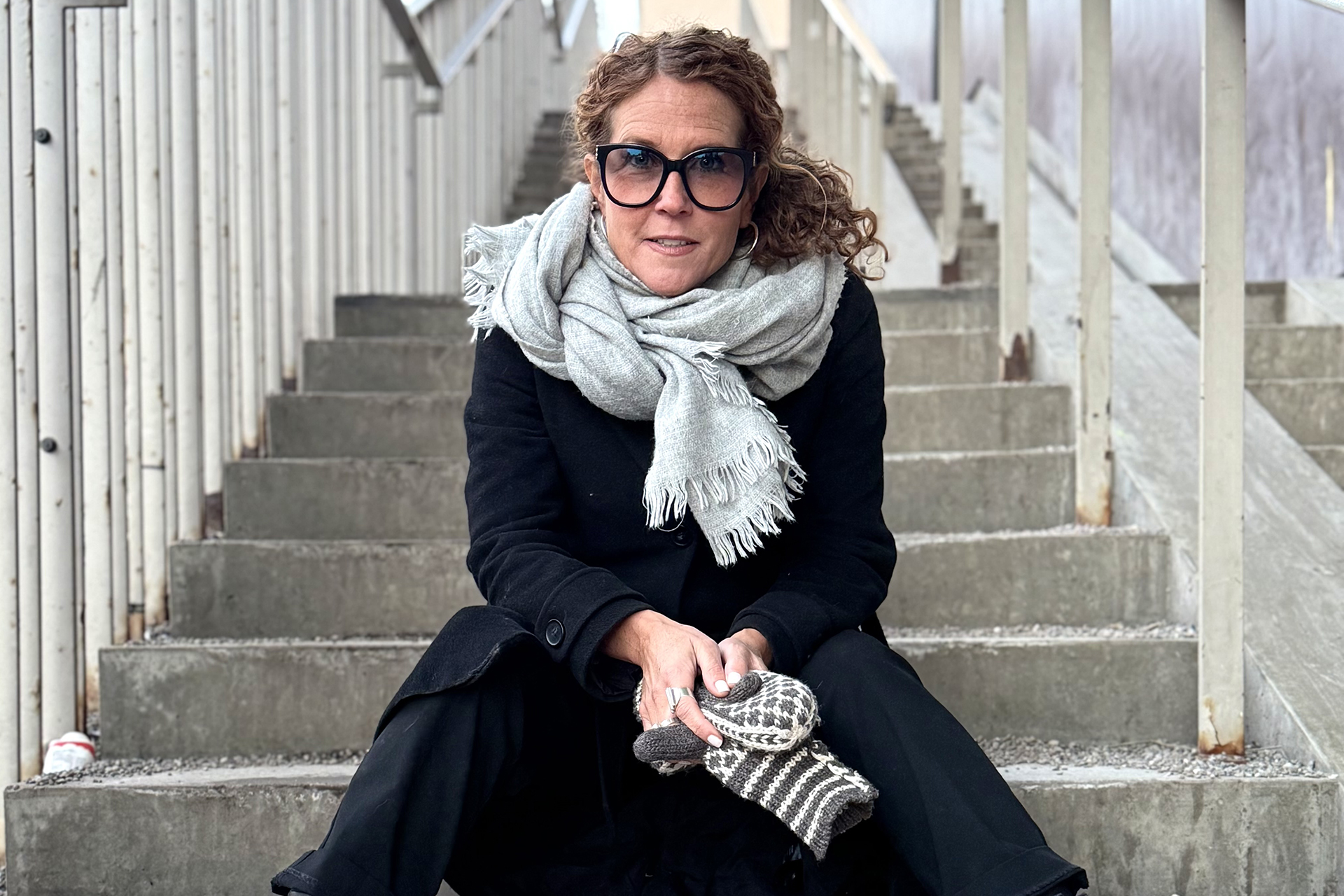 Porträttbild på Journalist Anna Lindman sittandes i en trappa. Vinter, utomhus i kappa, halsduk och solglasögn.