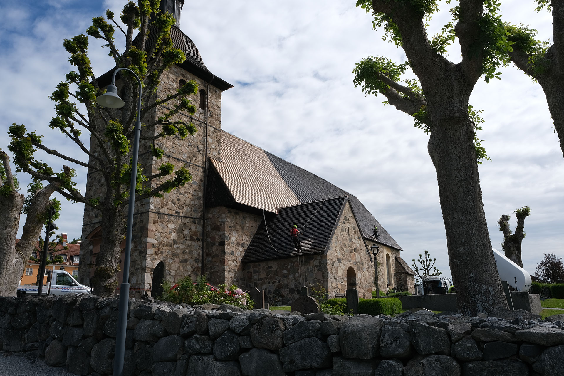 Två personer tjärar taket på Botkyrka kyrka. De hänger i rep 