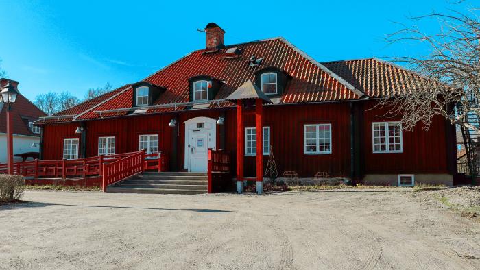 En faluröd träbyggnad med orange tegeltak. I bakgrunden en klarblå himmel. 