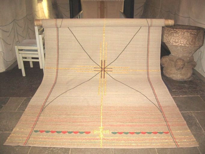 Bårtäcket i Järfälla kyrka utrullat på kyrkgolvet. Beige med kors broderat i guldtråd.