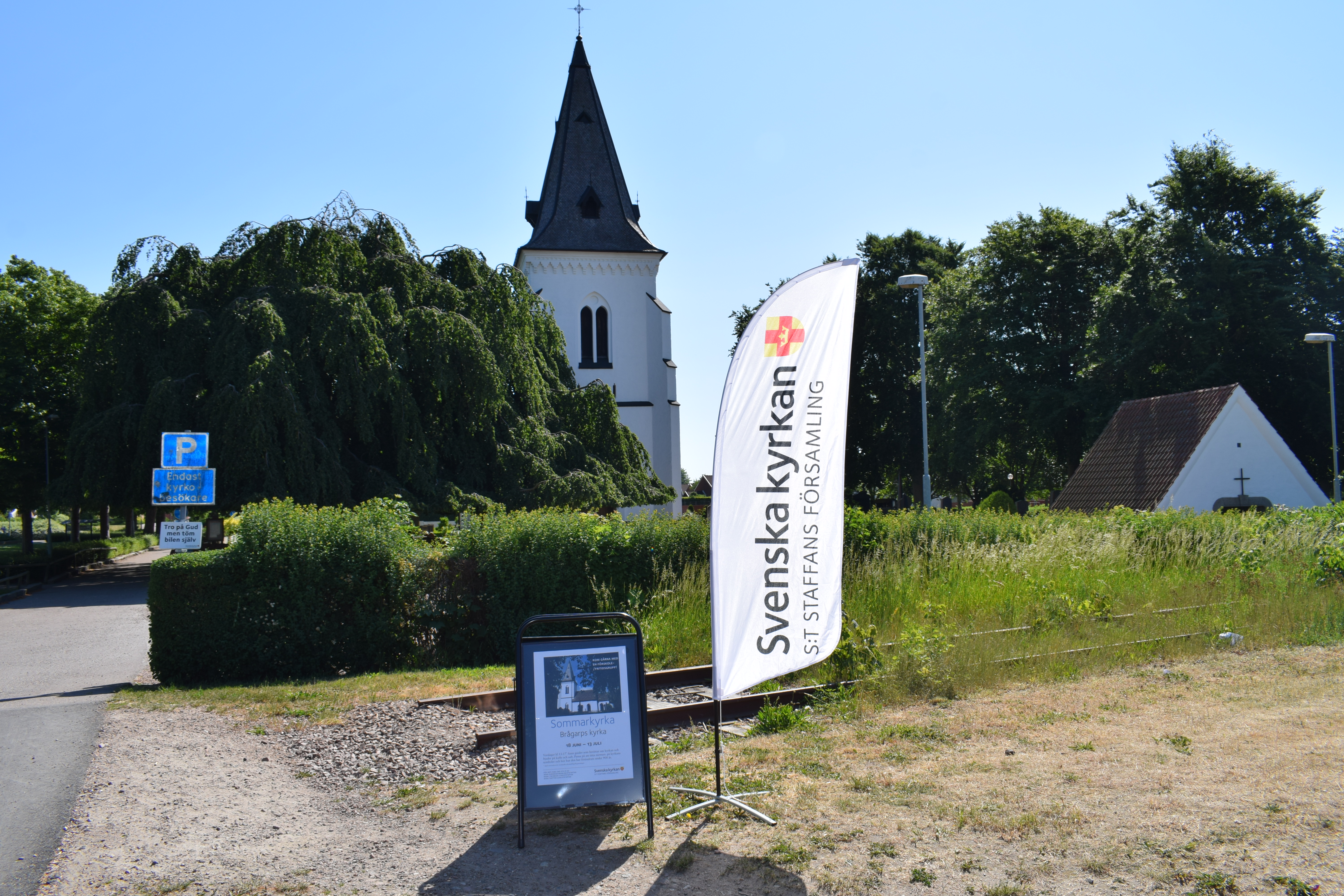 Gatuskylt och beach-flagga framför Brågarps kyrka, bjuder in till sommarkyrka.