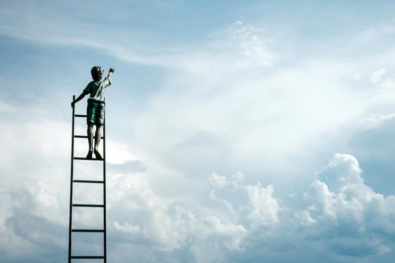 Pojke står på en stege och sträcker sig mot himlen.