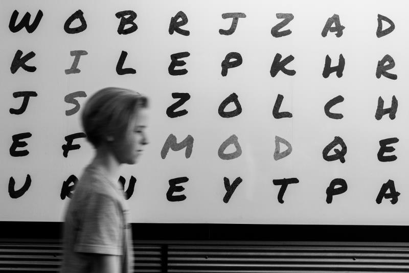 Pojke framför skylt med diverse bokstäver på.