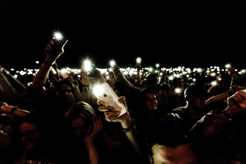 Folksamling som står i mörkret och håller upp sina tända mobilficklampor i luften.