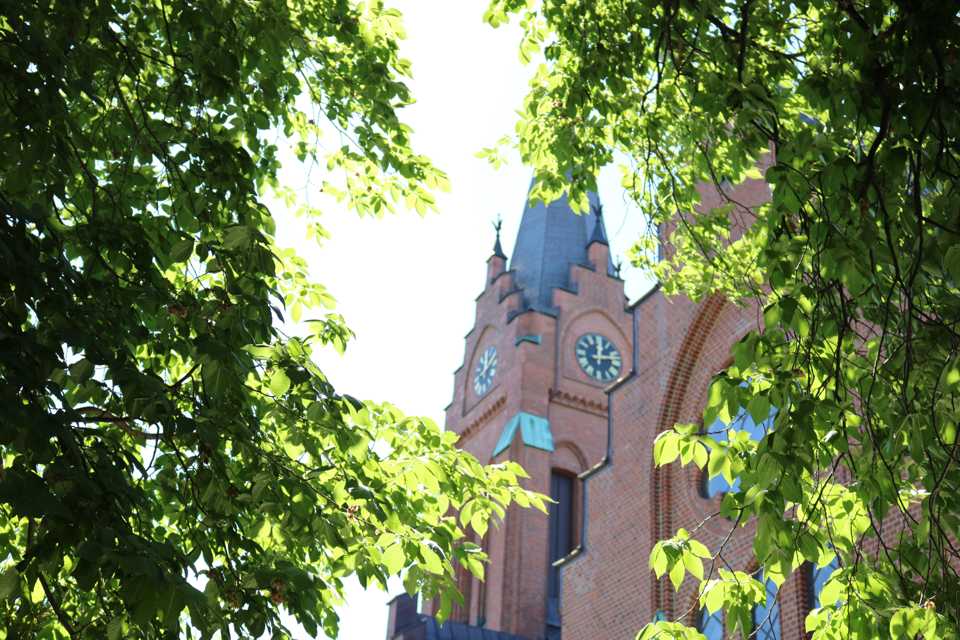Fässbergs kyrka torn syns genom bladverket.