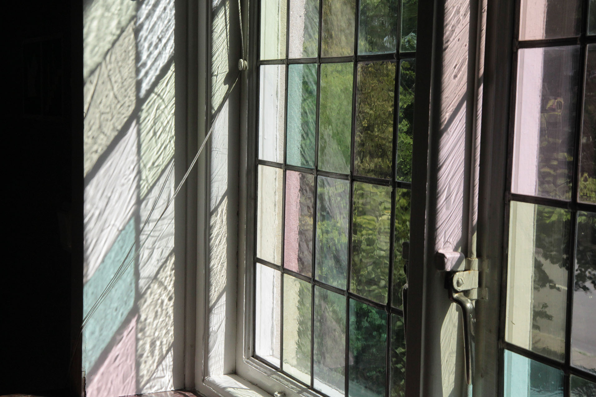 Ett gammaldags fönster med blyinfattade rutor. Solen faller in genom fönstret och rutorna bildar ett möster i pastellfärger på fönsterkarmen.