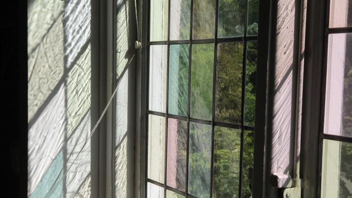 Ett gammaldags fönster med blyinfattade rutor. Solen faller in genom fönstret och rutorna bildar ett möster i pastellfärger på fönsterkarmen.