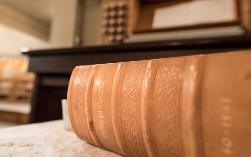 Beige äldre bibel på orgelpall framför kyrkorgel.
