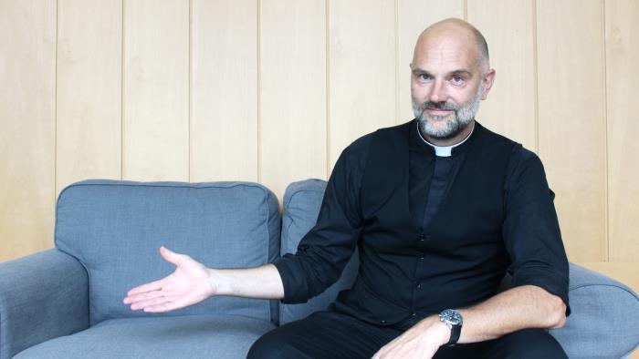 Kyrkoherde sitter i en blå soffa.