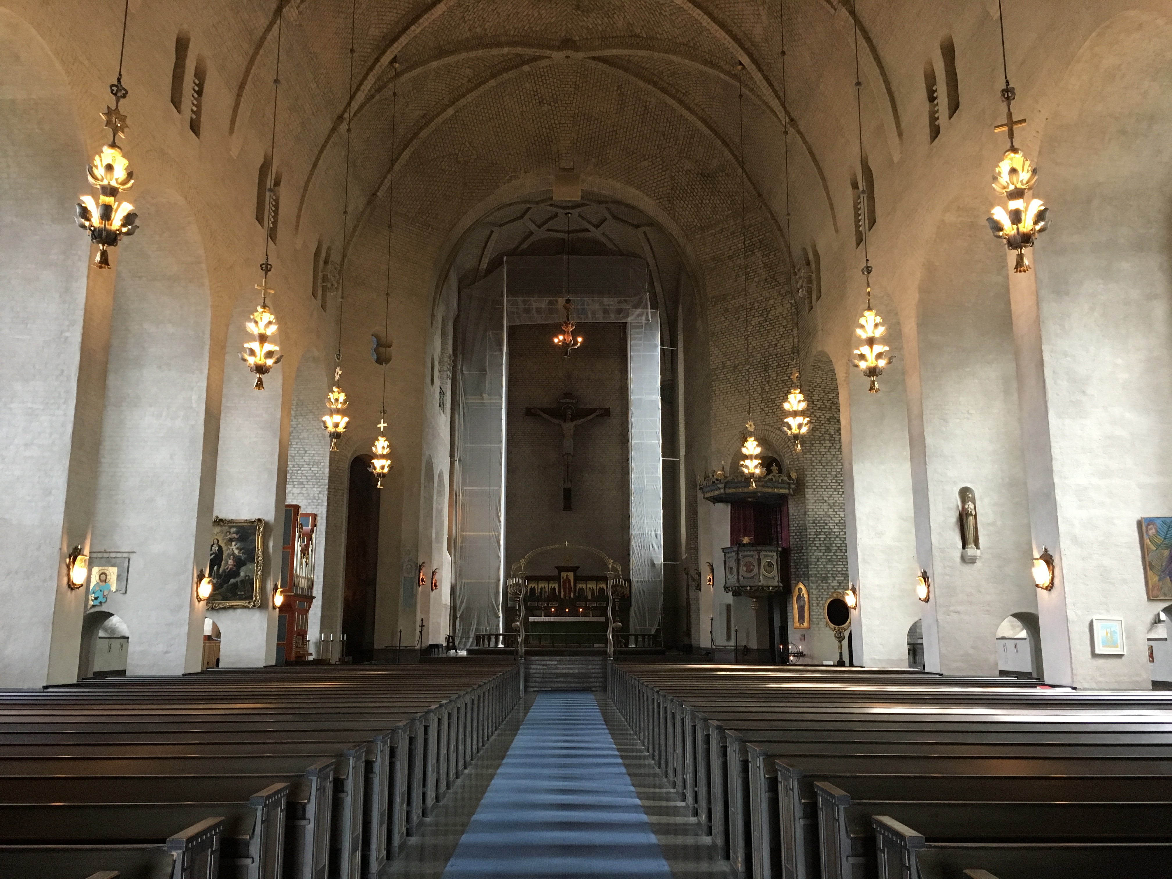 Inuti Högalidskyrkan, höga valv, lampor i tak och väggar, längst fram i kyrkan hänger ett stort kors med en skulptur av Jesus 