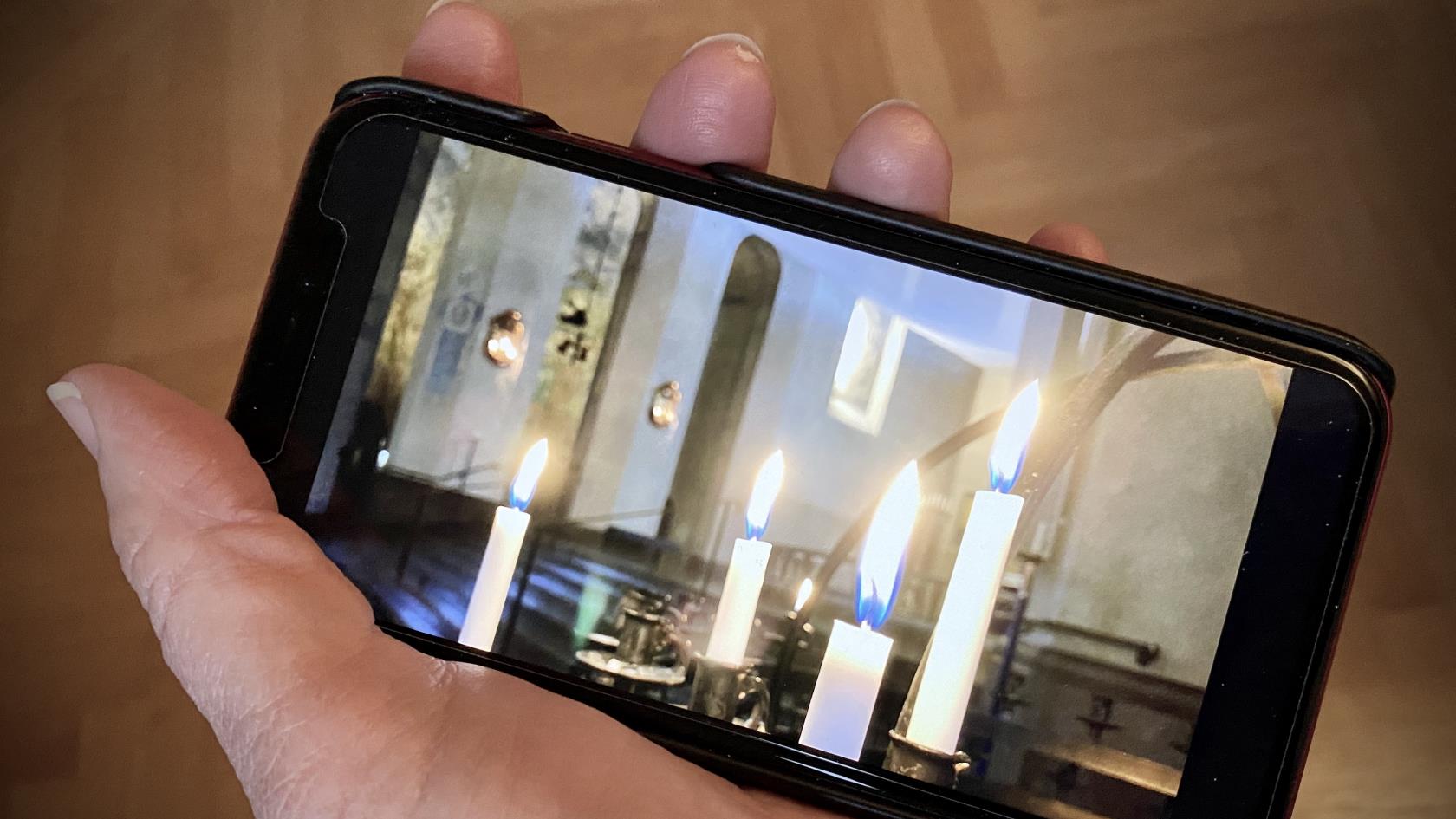 En hand håller i en mobil som ser ut att filma vita brinnande ljus i en kyrka. 