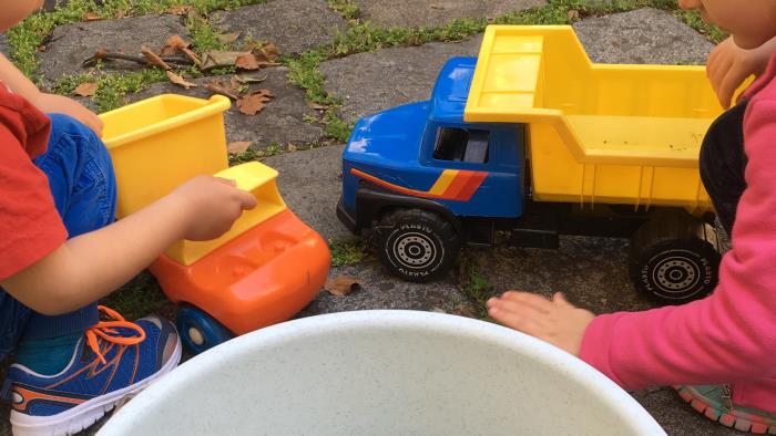 Barn ute på innergården leker med traktorer, lastbilar och en hink.