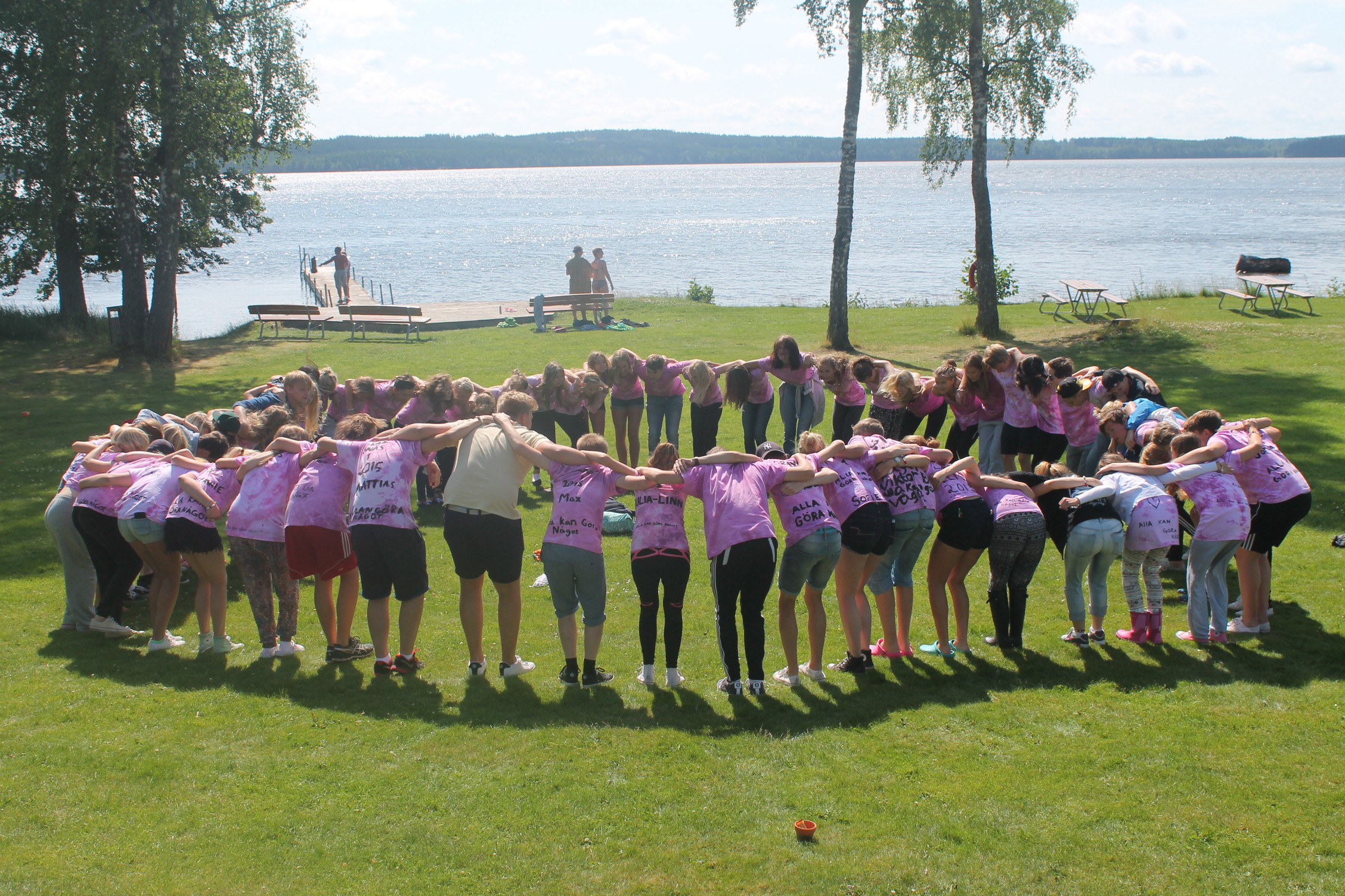 Ett drygt 40-tal ungdomar står i en cirkel på en gräsmatta och håller om varandra. 