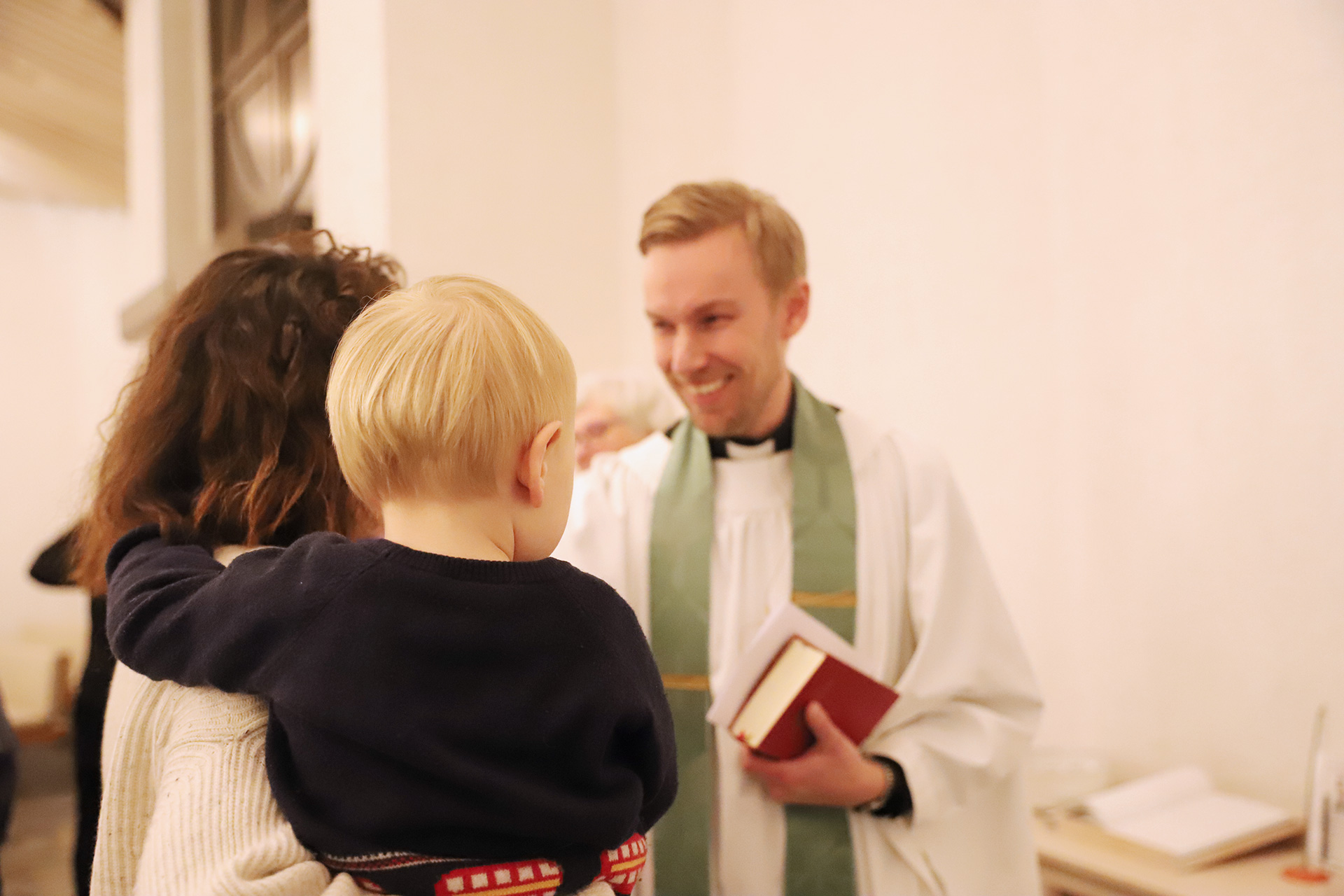 Präst hälsar på mamma med barn på armen.