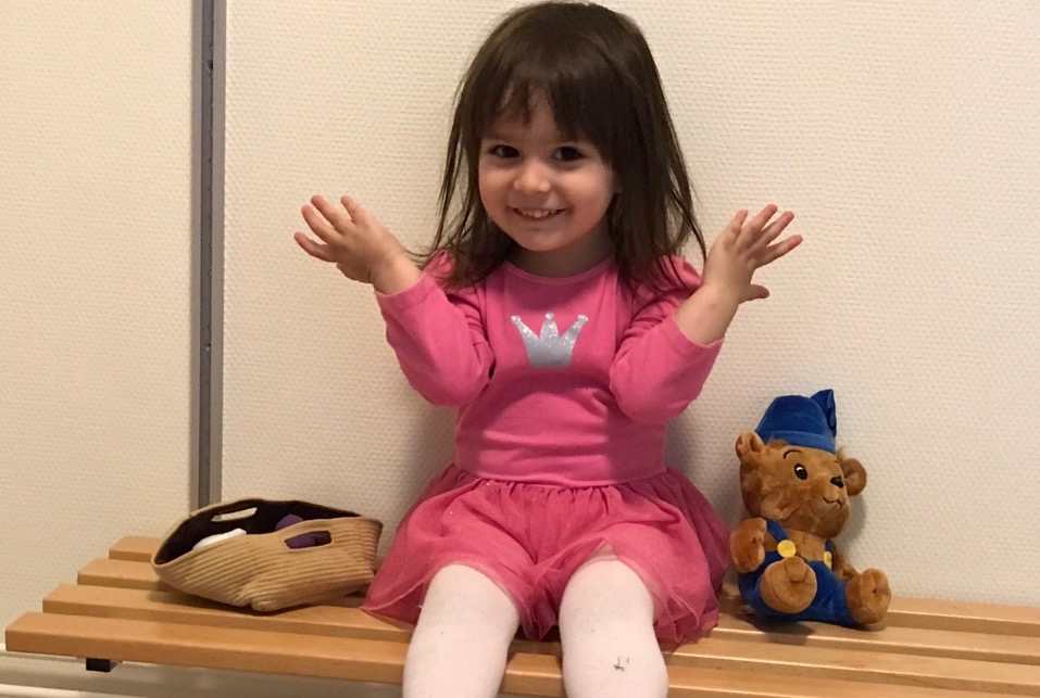 En glad liten flicka sitter på en bänk och lyfter på armarna. 