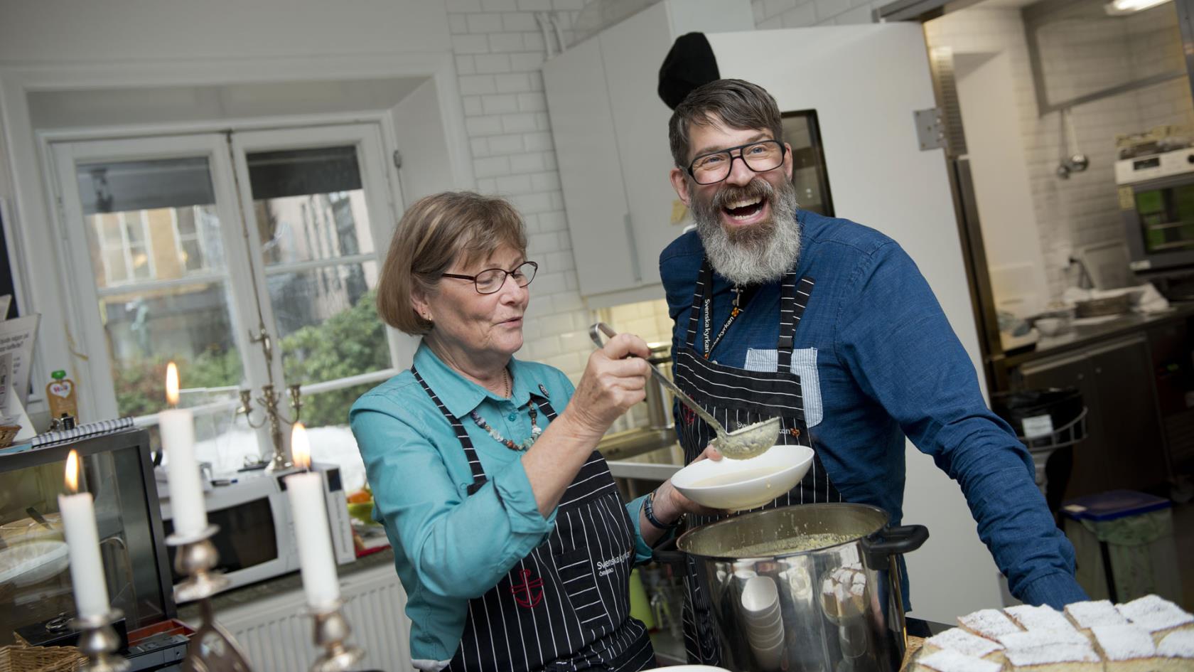 Bilden visar en glad husvärd/husmor Sonny Larsson i samspråk med en ideell medarbetare i Café Nikolai. 