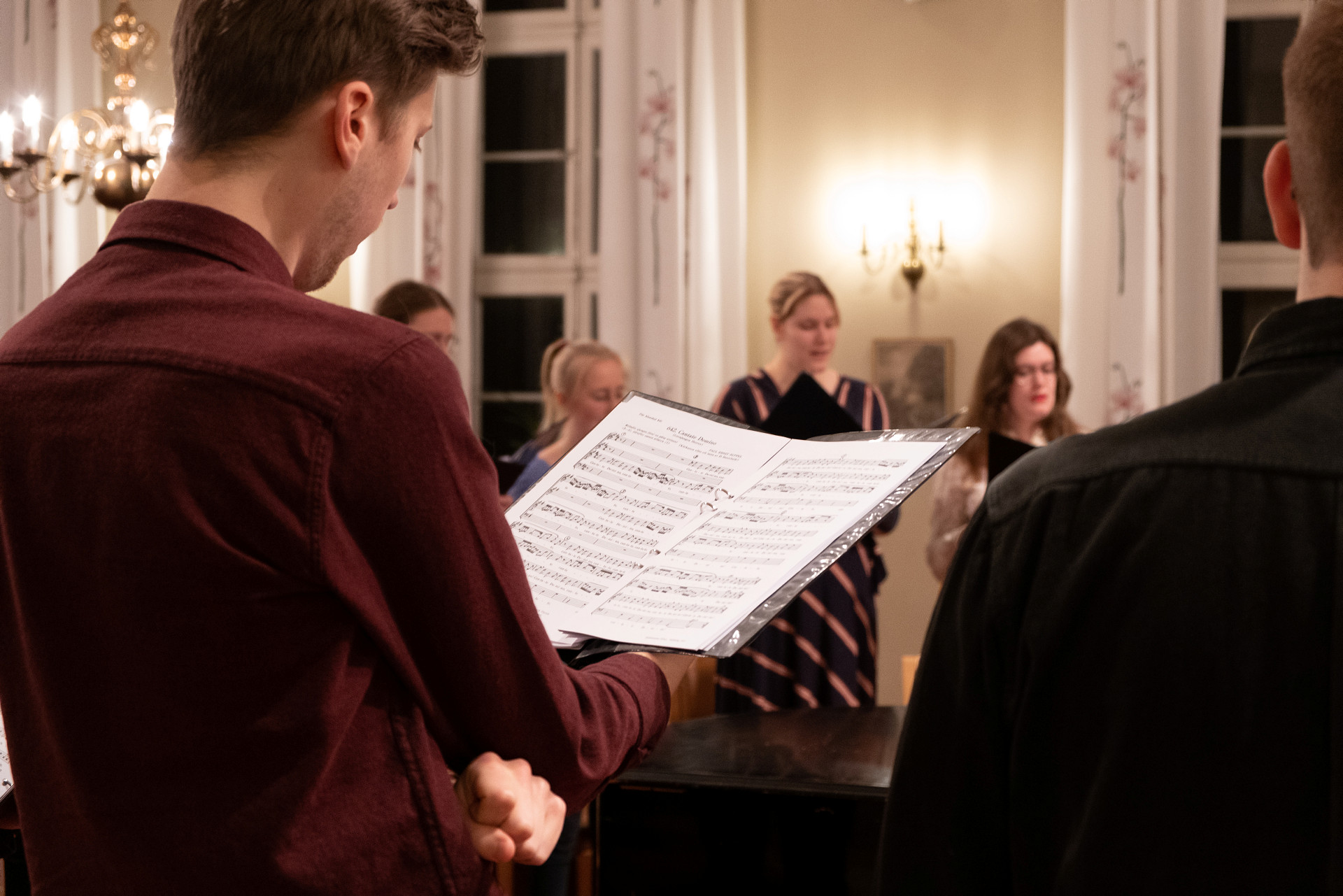 Människor står i halvcirkel och sjunger med noter i handen. 