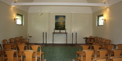 Inne i kapellet, vita väggar, stolar, ett bord.