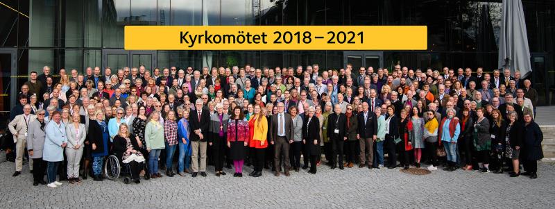 Kyrkomötets deltagare framför Uppsala konsert och kongress, med en skylt i bakgrund med texten: Kyrkomötet 2018-2022.