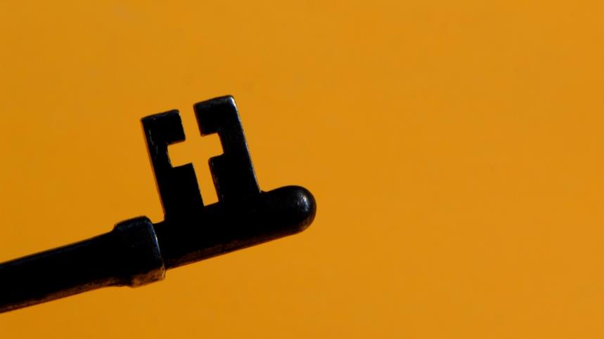 En nyckel i svart färg och en mörkgul bakgrund, nyckelns utskärning i axet är ett kors