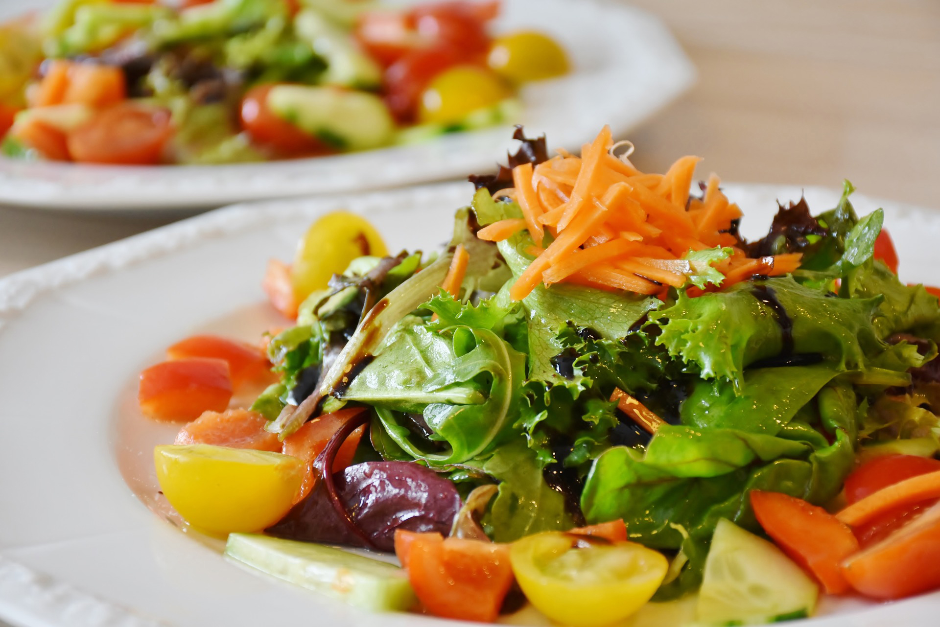 En vit tallrik med sallad, tomater, morot. 