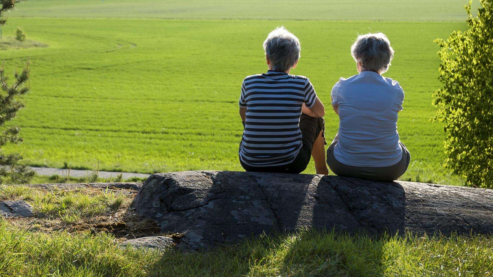Två kvinnor sitter på sten och tittar ut över grönt fält.