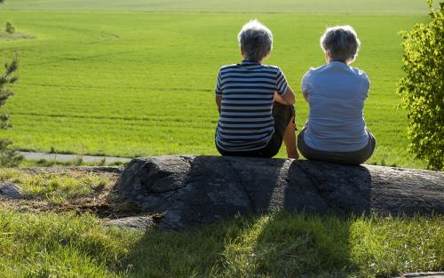 Två kvinnor sitter på sten och tittar ut över grönt fält.
