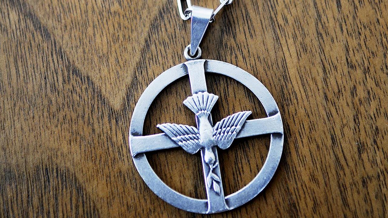 Diakonemblemet som utgörs av en ring, ett kors och en duva i ett halsband. 