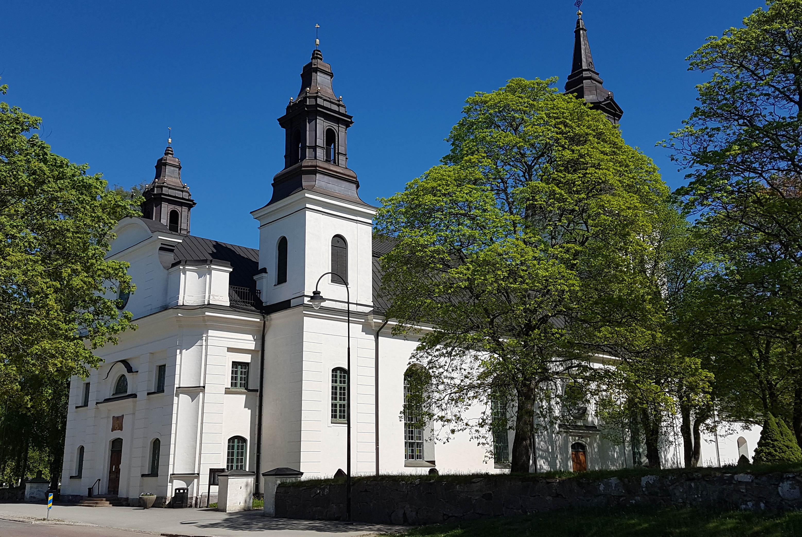 Vit kyrka med svart tak och några träd som grönskar