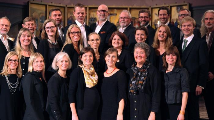 Gruppbild av Oscar Fredriks Kammarkör, alla är mörkt klädda och ler in i kameran.