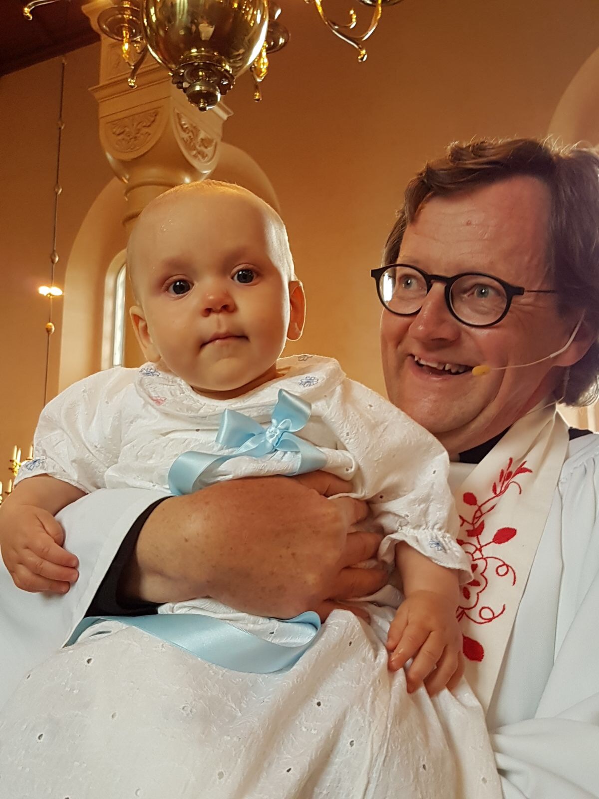 Barn i dopklänningen i famnen på en präst