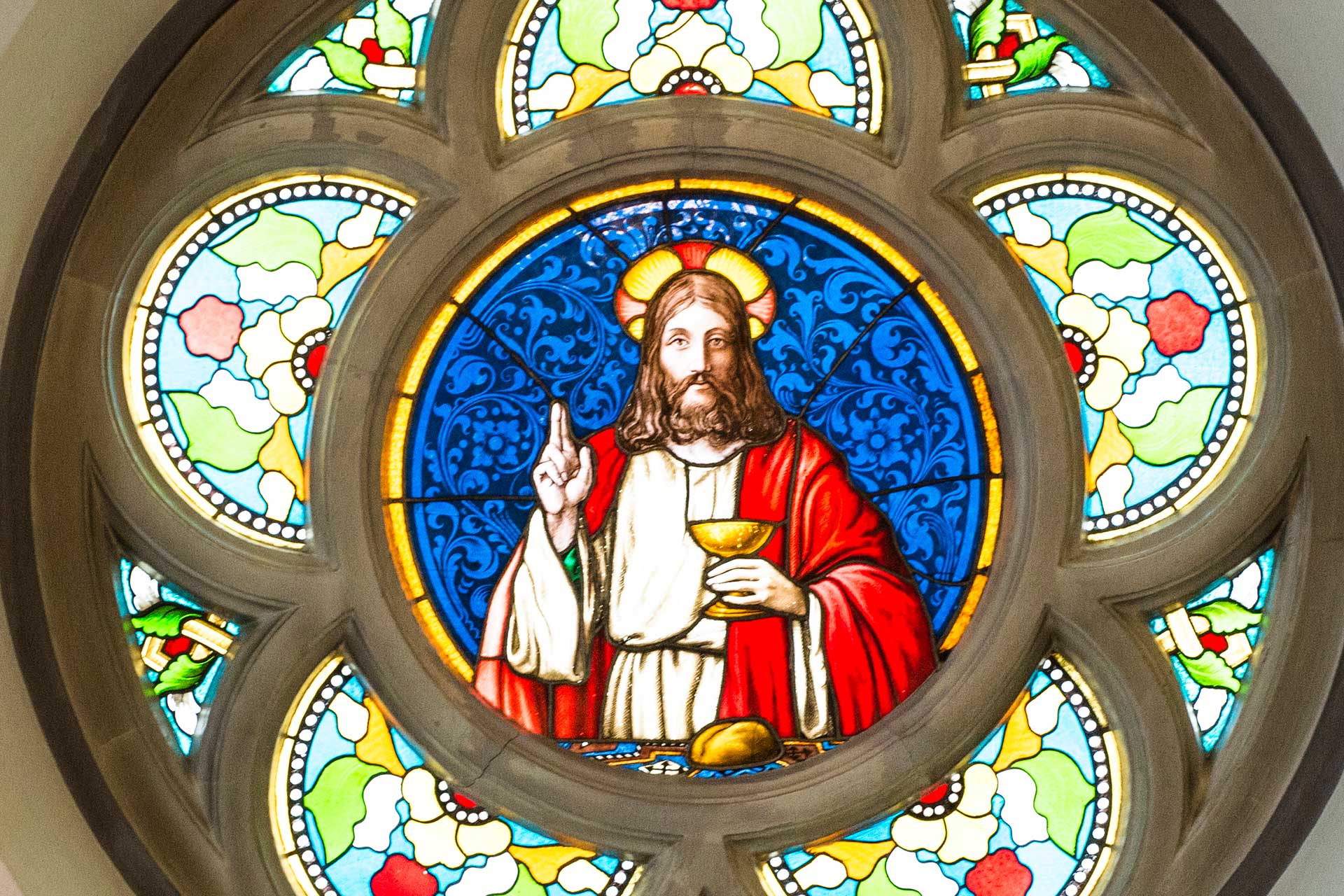 Rosettfönster med glasmålningar föreställande en välsignande Jesus i mitten.