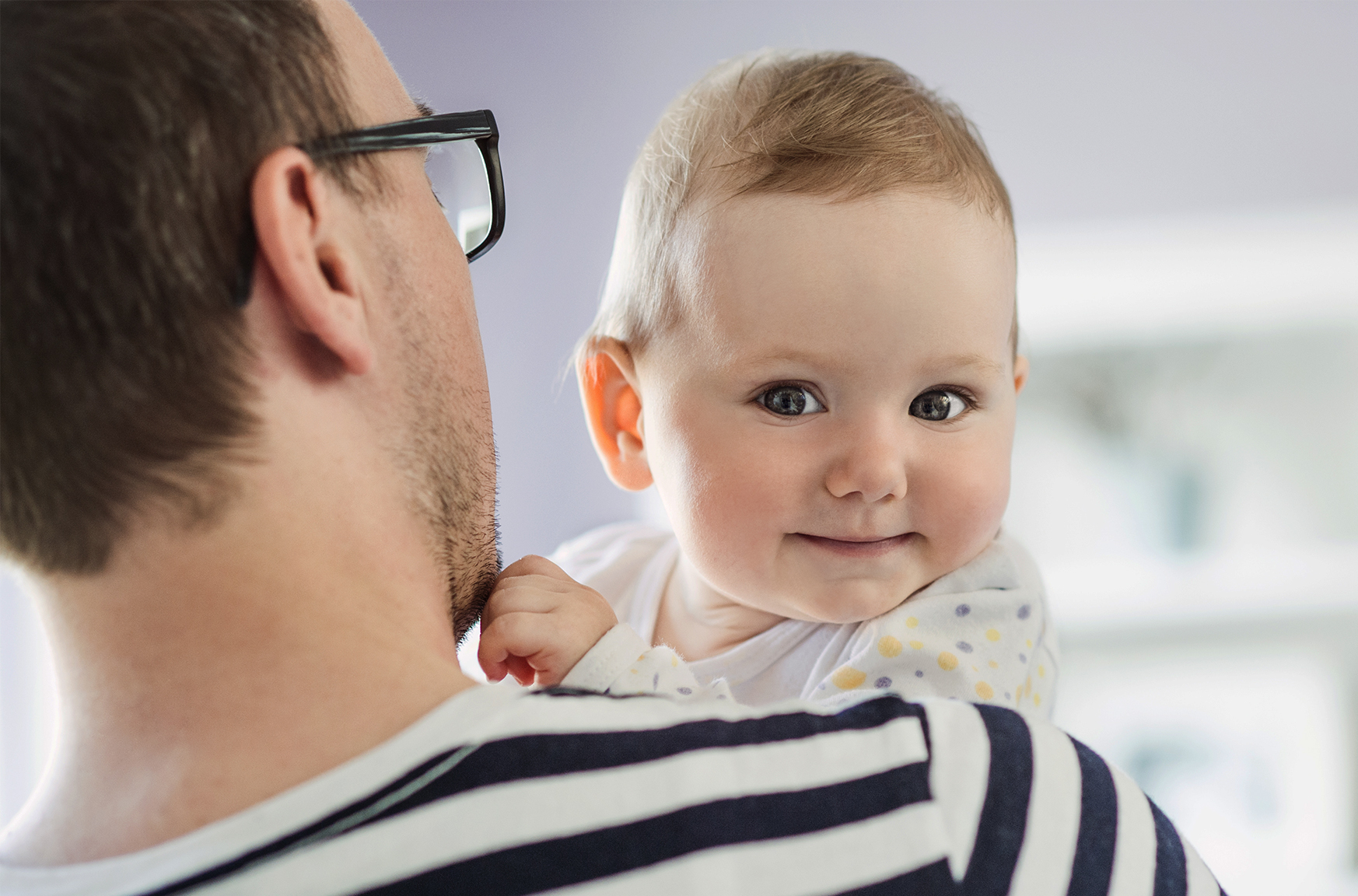 En person i glasögon håller i en bebis som ser glad ut. 
