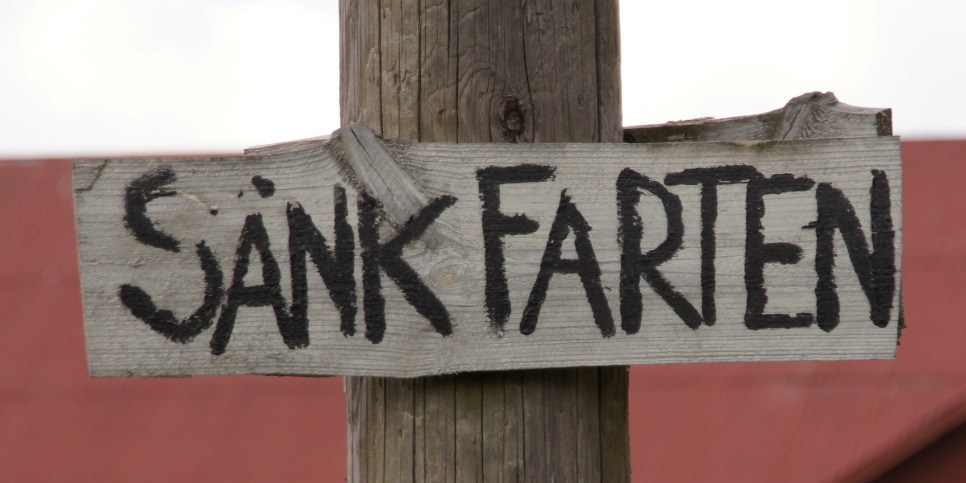 En träskylt med texten "Sänk farten"